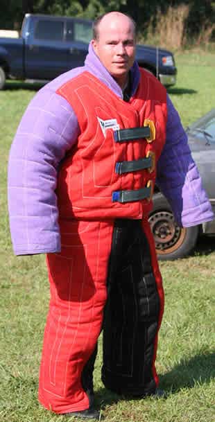 Person wearing an oversized padded suit outdoors, standing on grass with vehicles in the background.